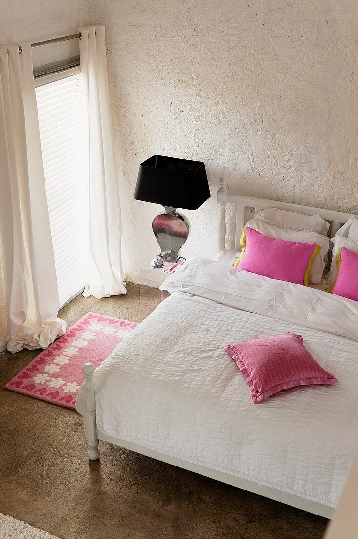 Pink cushions on white bed in bedroom with pink carpet