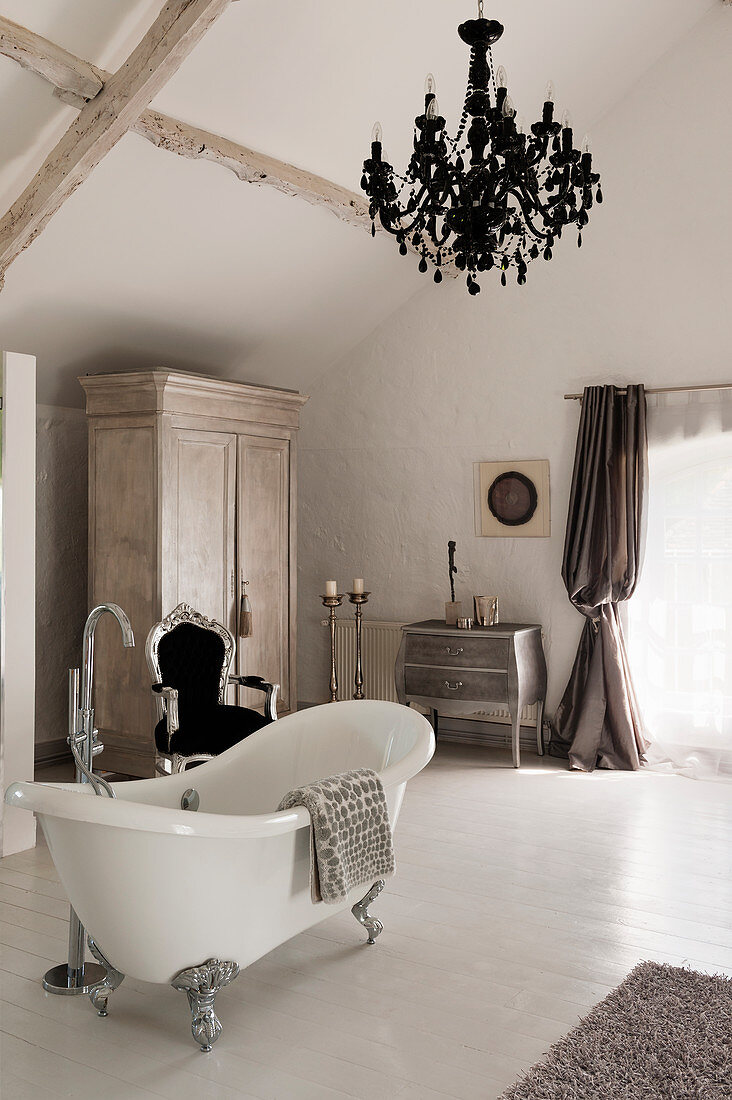 Freistehende Badewanne im Zimmer mit französischer Kommode, silber geschnitztem französischem Stuhl und schwarzem Kronleuchter