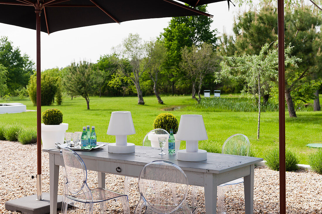 Gartenleuchten auf Holztisch mit Klassikerstühlen unter Sonnenschirm im Garten