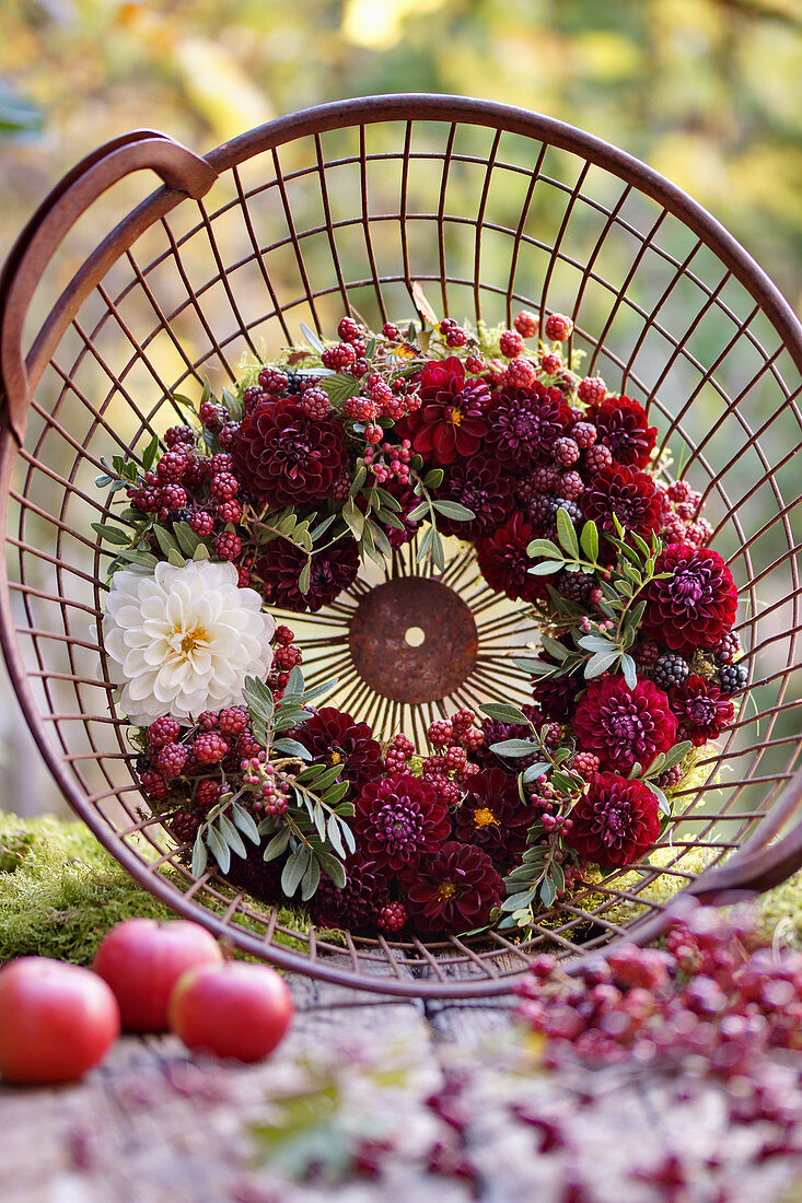 Wreath of dahlias, unripe blackberries and mastic pistachio in a harvest basket