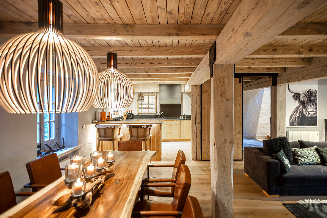 Windlichter auf Esstisch aus Holz in offenem Wohnraum mit Holzdecke