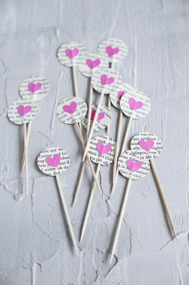 Toothpicks decorated with circles of book pages and pink paper hearts