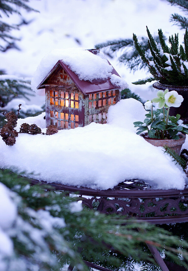 Schnee auf einem beleuchteten Deko-Häuschen im Garten