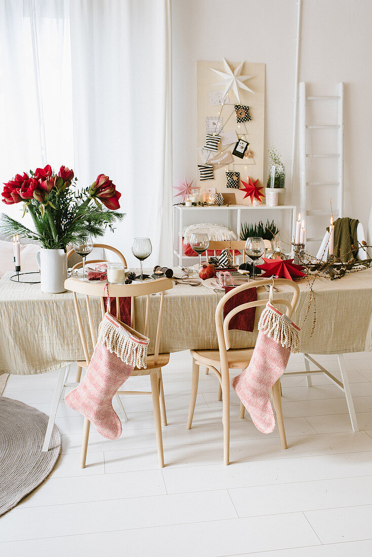 Table set for Christmas meal with vase of amaryllis and stockings hung from chair backs