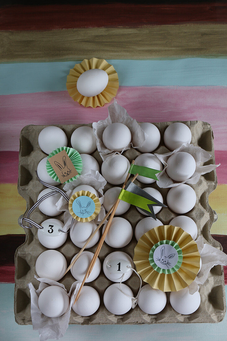 Papierrosetten und kleine Fahnen auf einer Eierpalette mit weißen Eiern