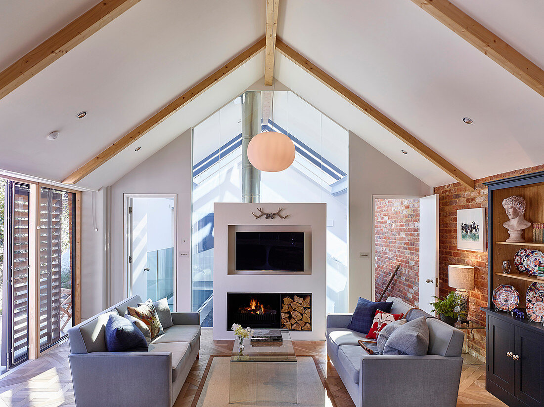 Grey sofas and modern open fireplace in living room below pitched roof