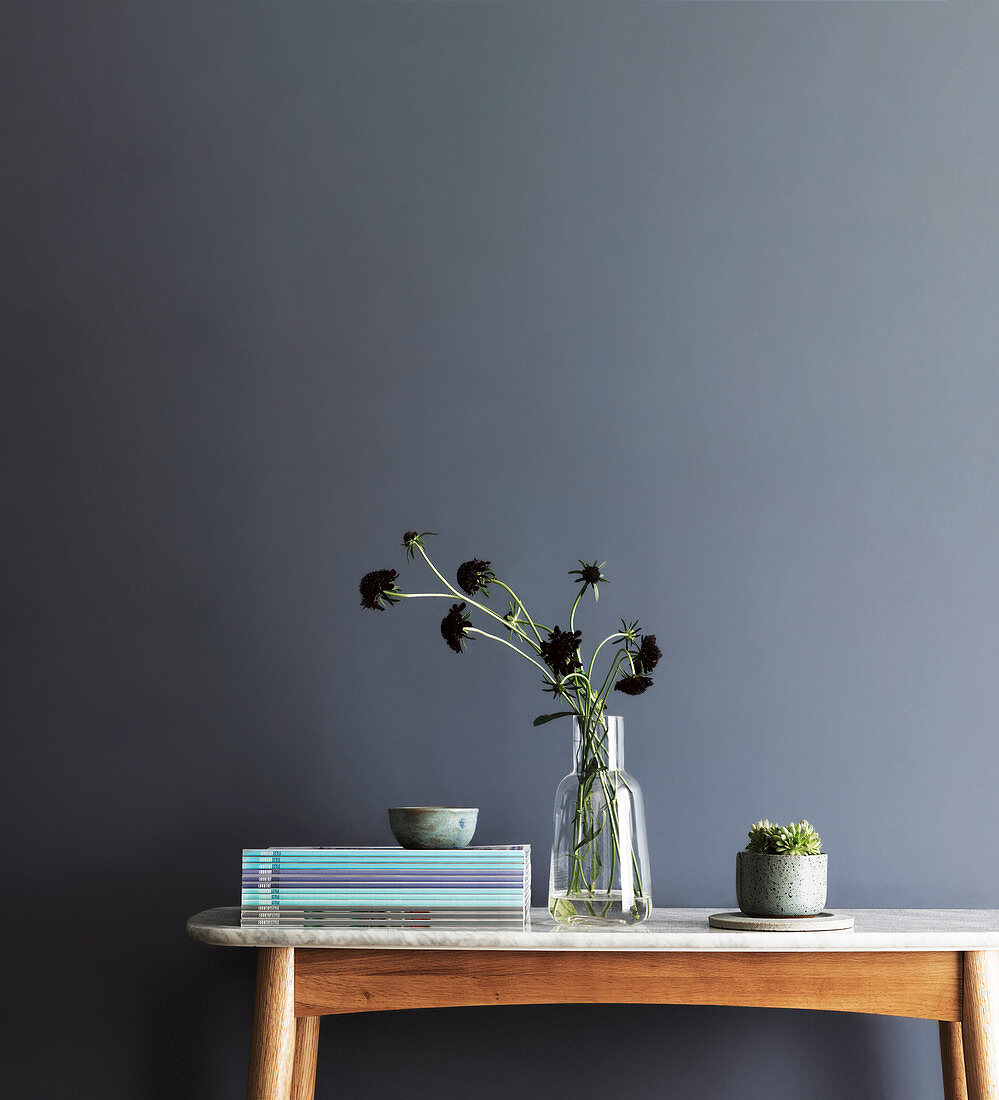 Stapel Zeitschriften und Vasse auf dem Tisch vor blaugrauer Wand