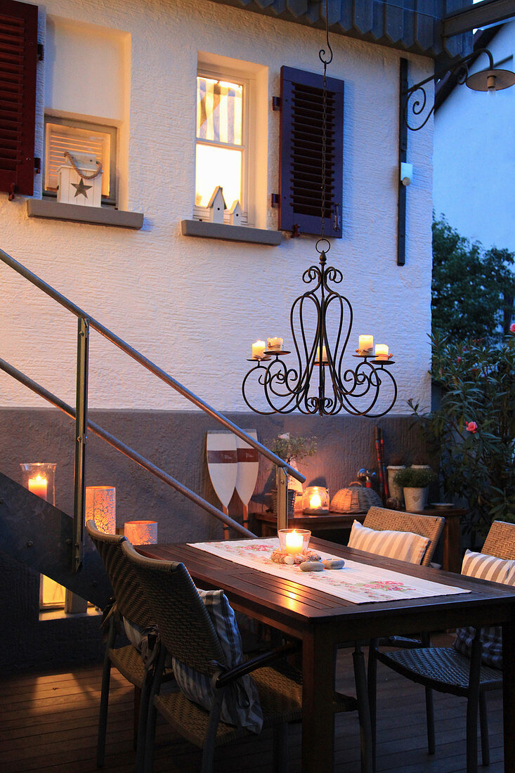 Table and chairs with tealights and candle chandelier on twilight terrace