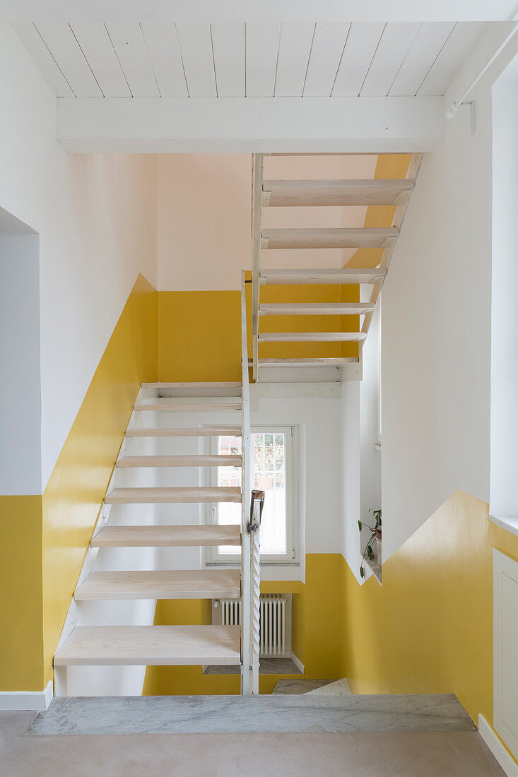 Weißes Treppenhaus mit halbhoch gelb gestrichener Wand