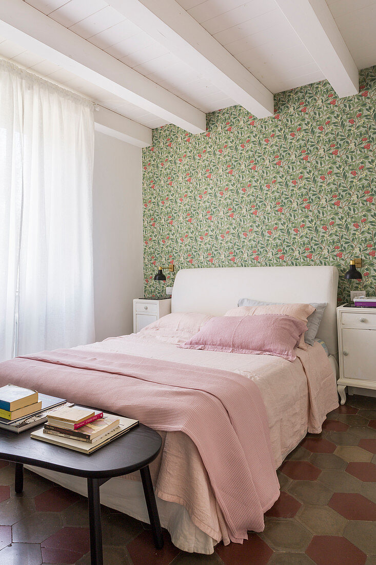 Bed against vintage-style floral wallpaper in bedroom with ceiling beams