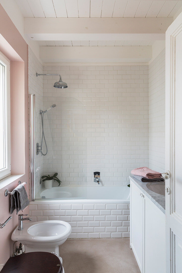 Bathtub clad with subway tiles in small bathroom with pink wall