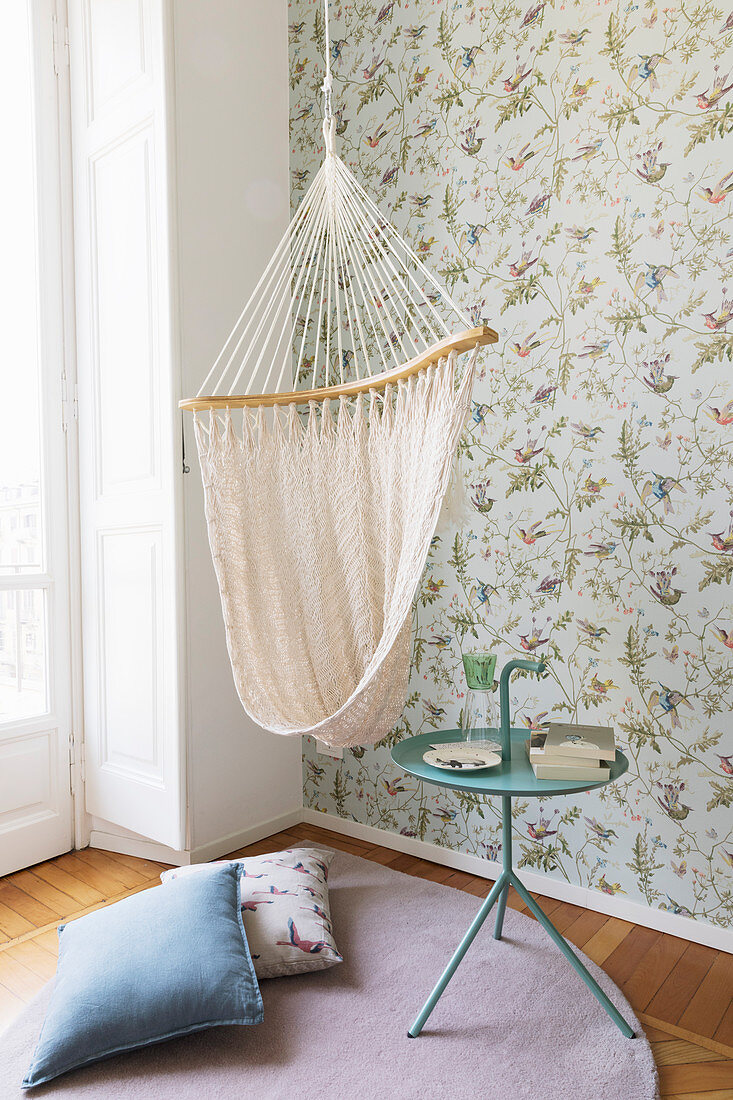 Hanging chair and side table in front of vintage-style floral wallpaper