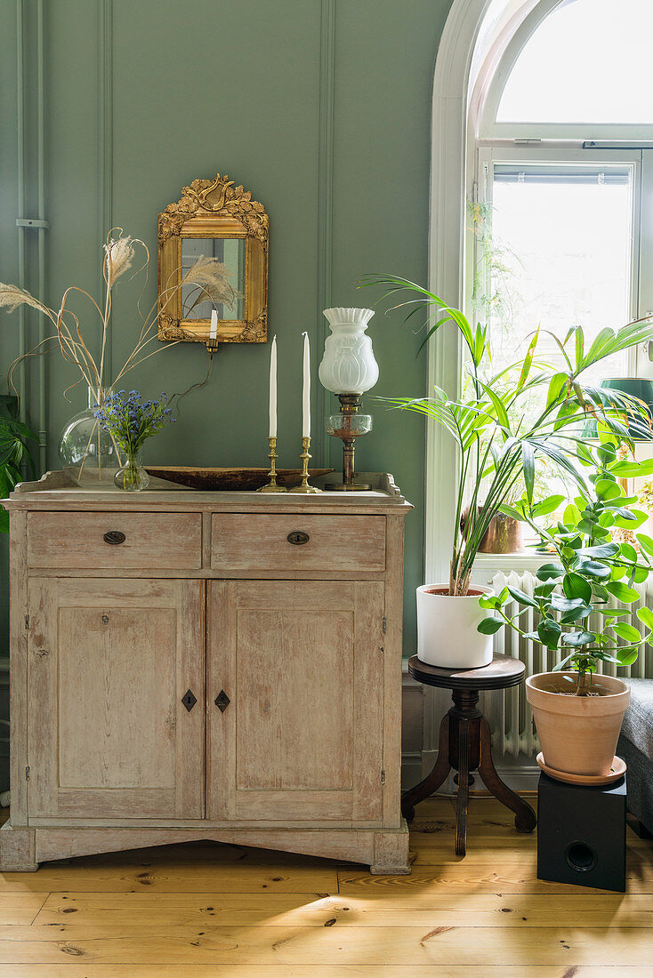 Vase, candles and paraffin lamp on cabinet against green wall