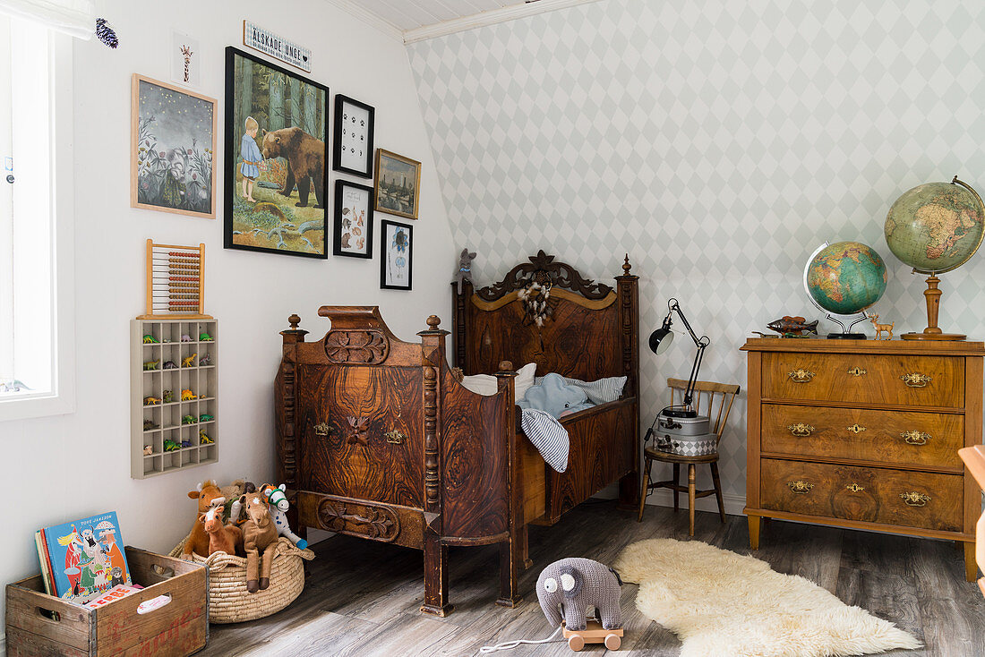 Antique bed and chest of drawers below paintings on wall in child's bedroom