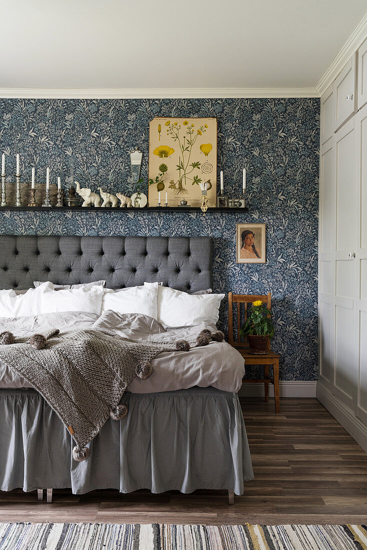 Double bed with button-tufted headboard and blue-patterned wallpaper in bedroom