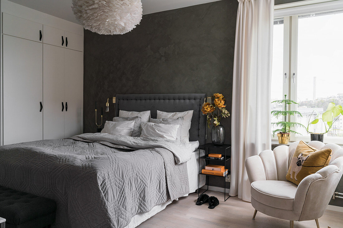 Doppelbett, weißer Kleiderschrank und Sessel im Schlafzimmer mit dunkelgrauer Wand