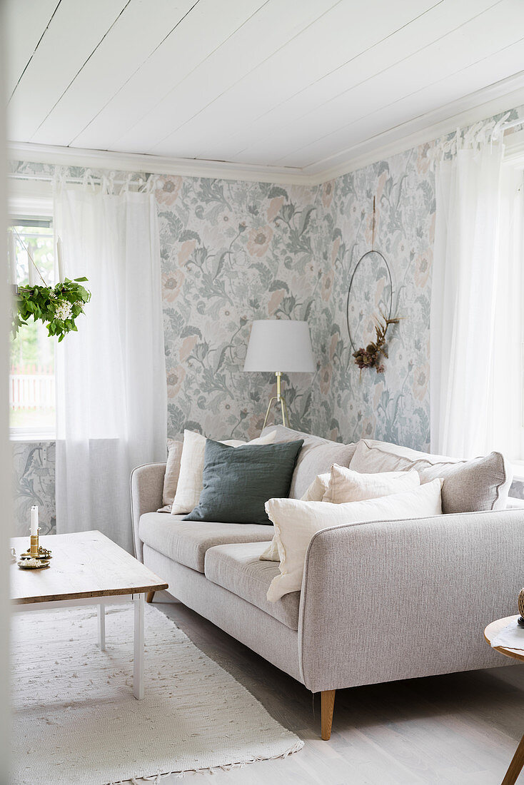 Pale sofa with scatter cushions in living room with floral wallpaper