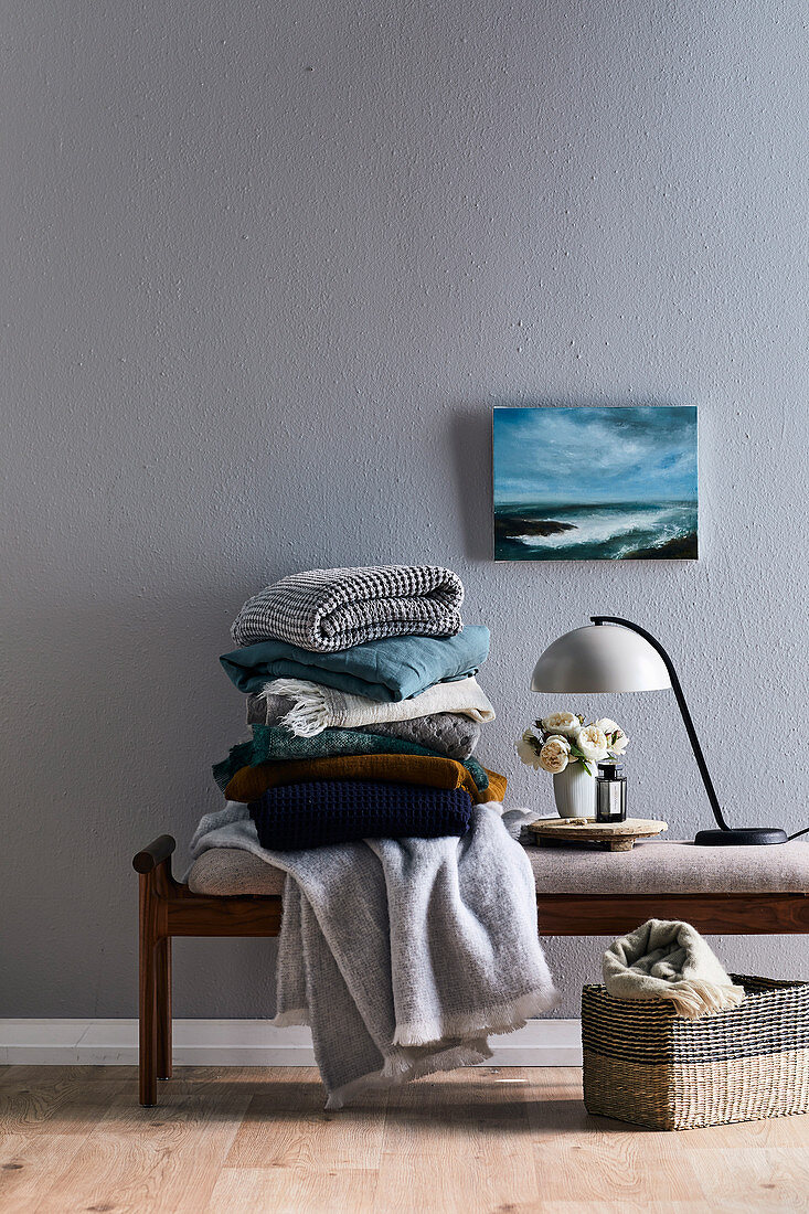 Stack of soft blankets on an upholstered bench in front of a grey wall