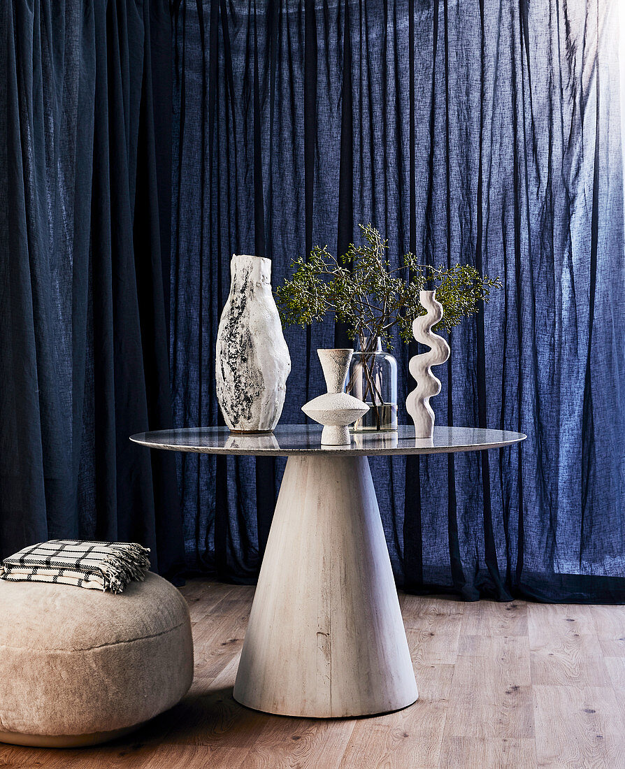 Verschiedene Vasen auf rundem Tisch vor dunkelblauem Vorhang