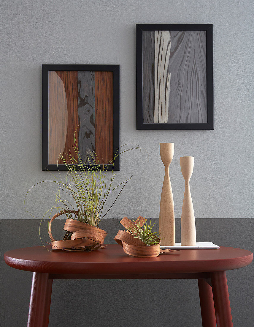 Bilder aus Furnierholz an grauer Wand, Tisch mit skulpturalen Vasen