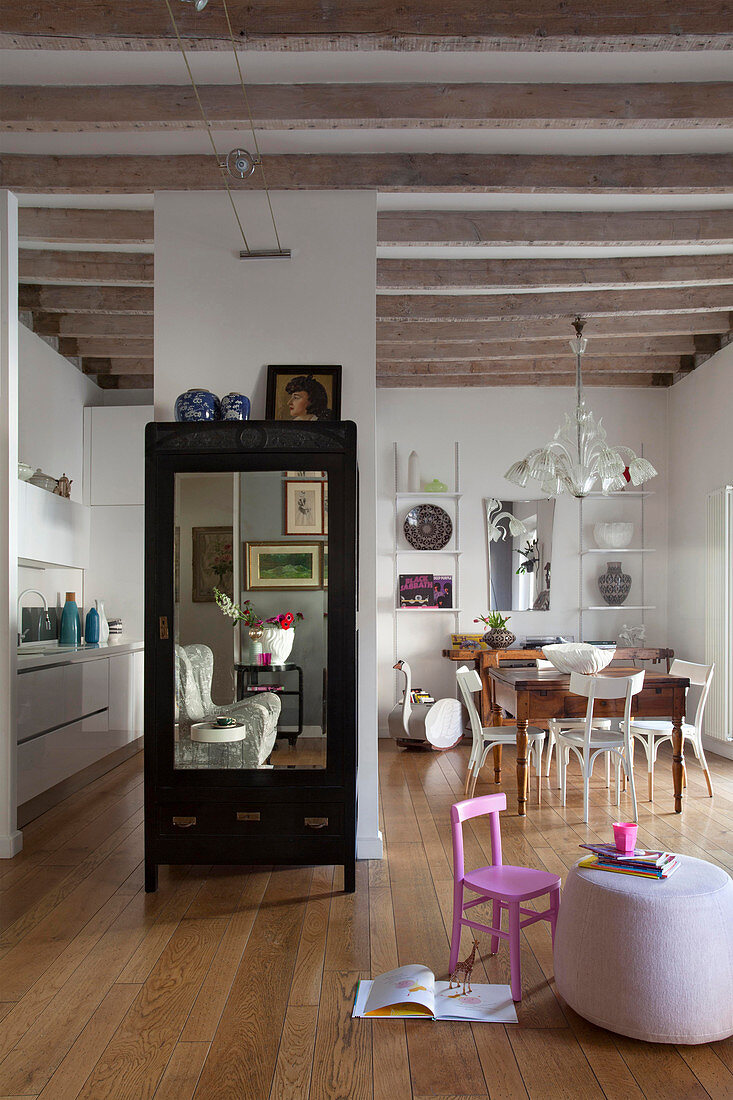 Cupboard with mirrored door in open-plan interior with wood-beamed ceiling
