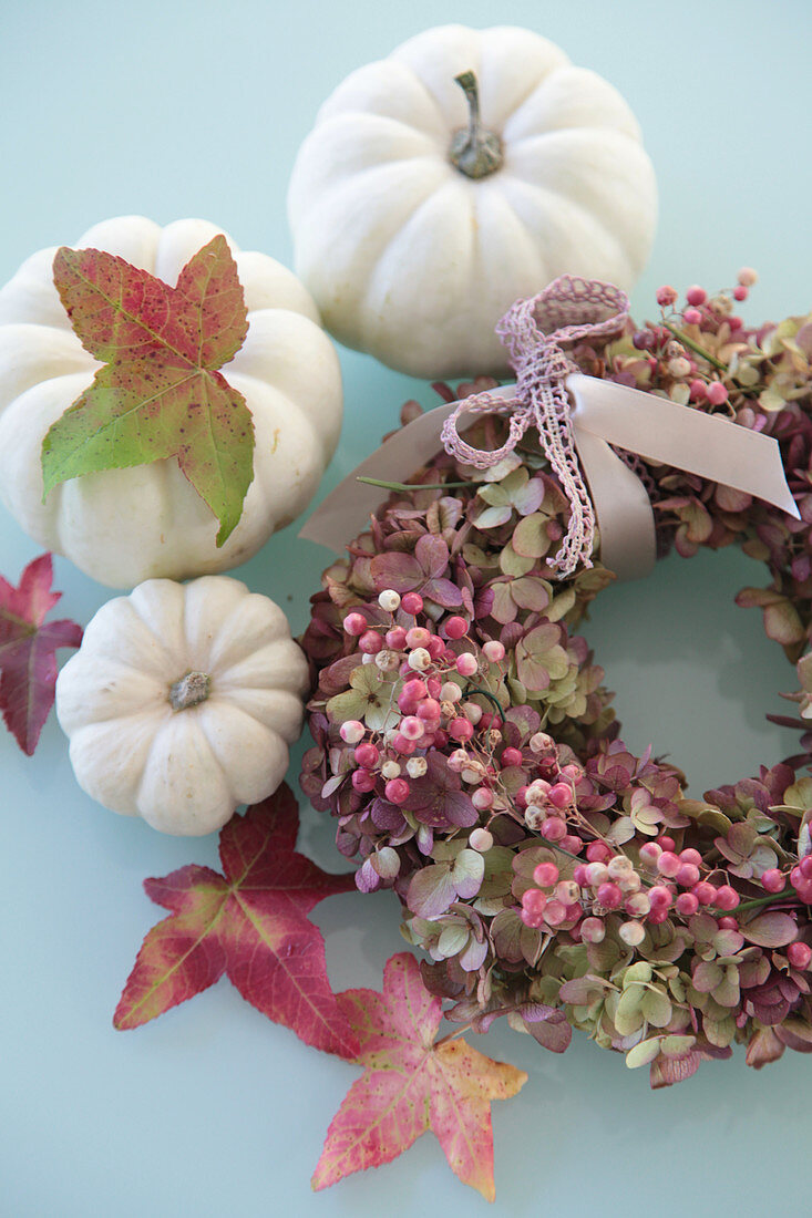 White pumpkins, sweetgum leaves and wreath of hydrangea flowers and pink pepper