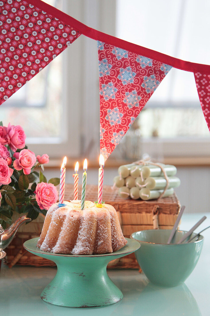 Geburtstagstisch mit Kuchen mit Kerzen, Girlande und Rosen