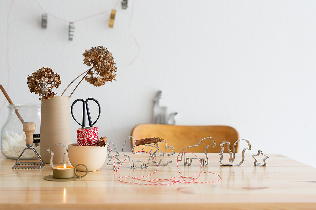 Plätzchenausstecher, Garn, Teelicht und Vase mit Trockenblume auf Tisch