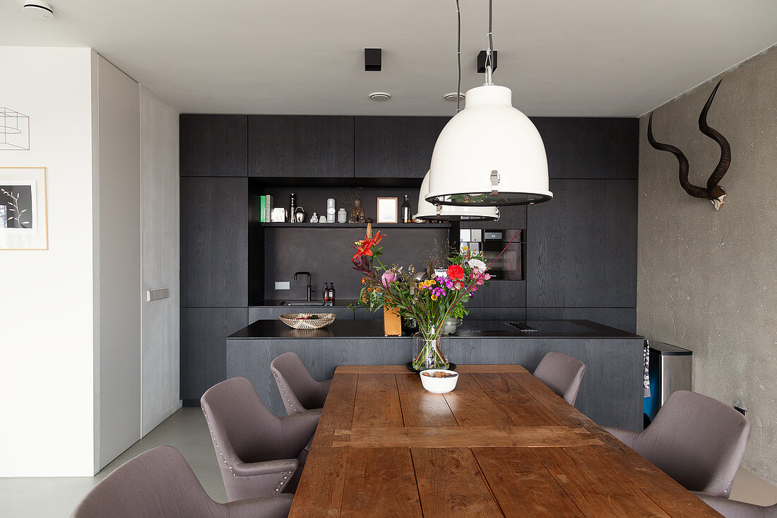 Dining table with solid wooden top and elegant chairs in front of kitchen with dark cabinets