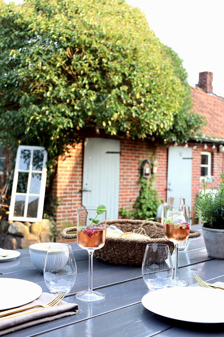 View across table set with glasses of wine to outbuildings with ivy-covered roof