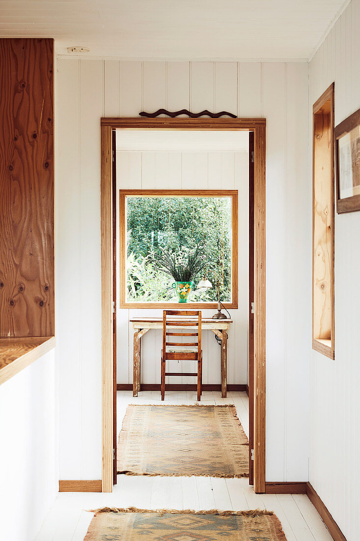 Blick durch geöffnetes Tür auf kleinen Schreibplatz vor Fenster mit Gartenblick