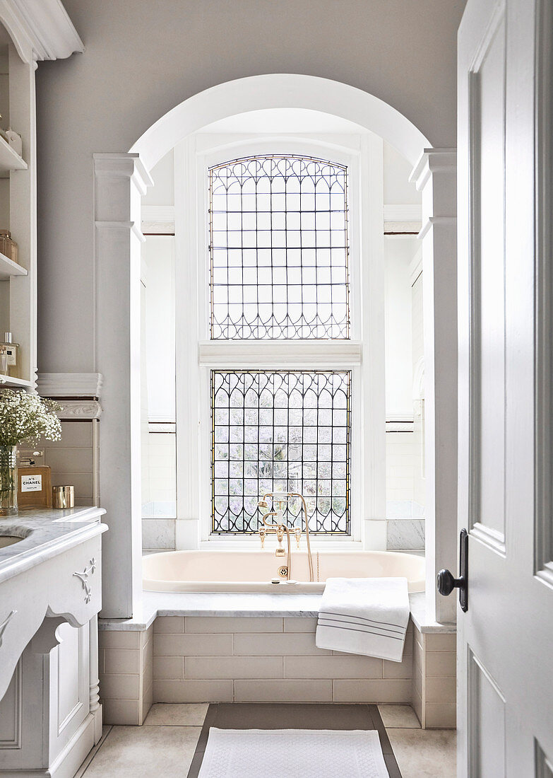 View into the bathroom with ornate window above the bathtub