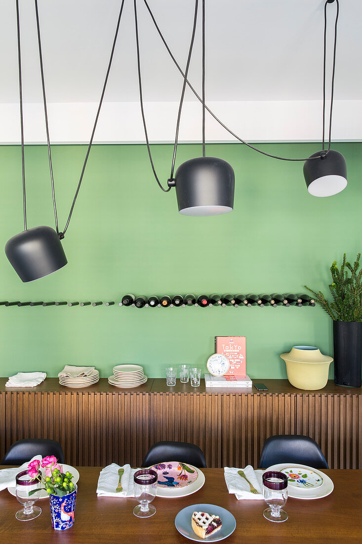 Edler Tisch aus Nussbaumholz, Pendelleuchten und Sideboard im Esszimmer mit grüner Wand
