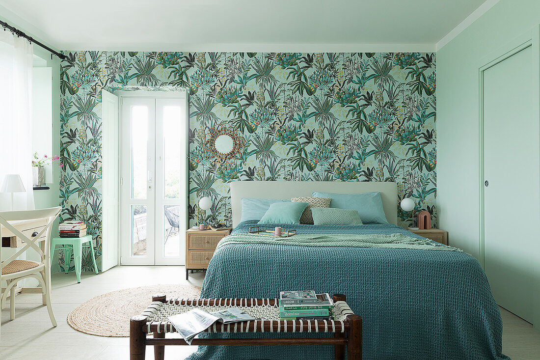 Doppelbett mit Tagesdecke und Bank im Schlafzimmer, Tapete mit Pflanzenmotiv