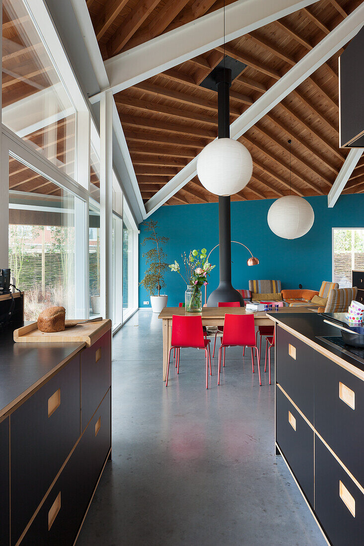 Helles Esszimmer mit blauer Wand, roten Stühlen und Holzbalkendecke