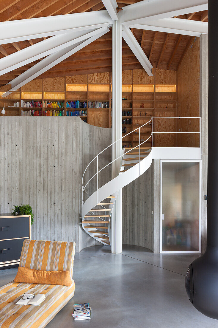 High living room with spiral staircase, exposed concrete wall, beamed ceiling and wooden shelving in the gallery