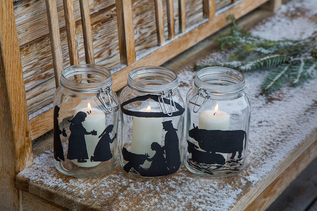 White candles in mason jars painted with festive silhouettes