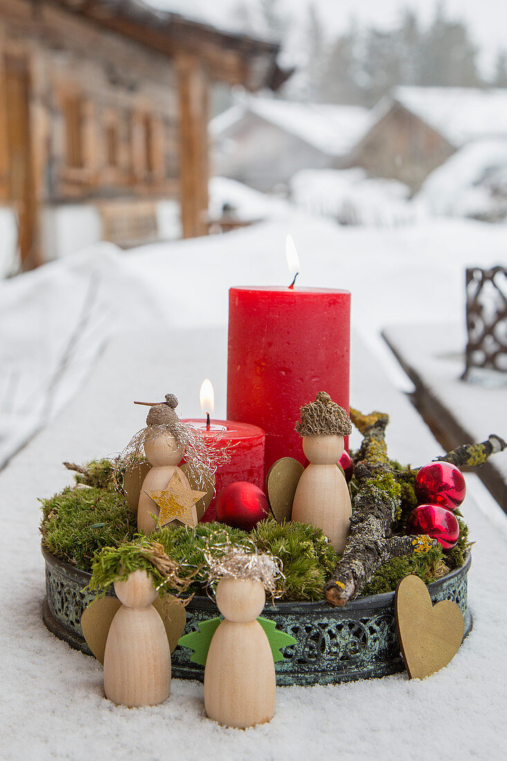 Red candle and small wooden angels on tray of moss in snow
