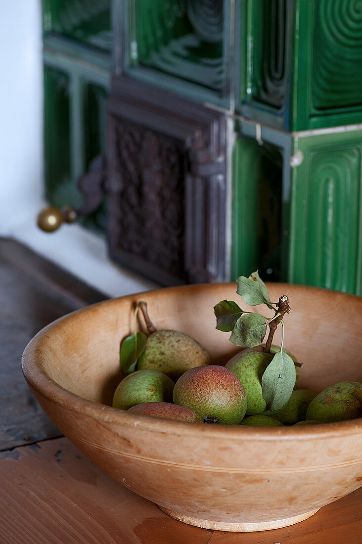 Pears in wooden bowl on bench around green tiled stove