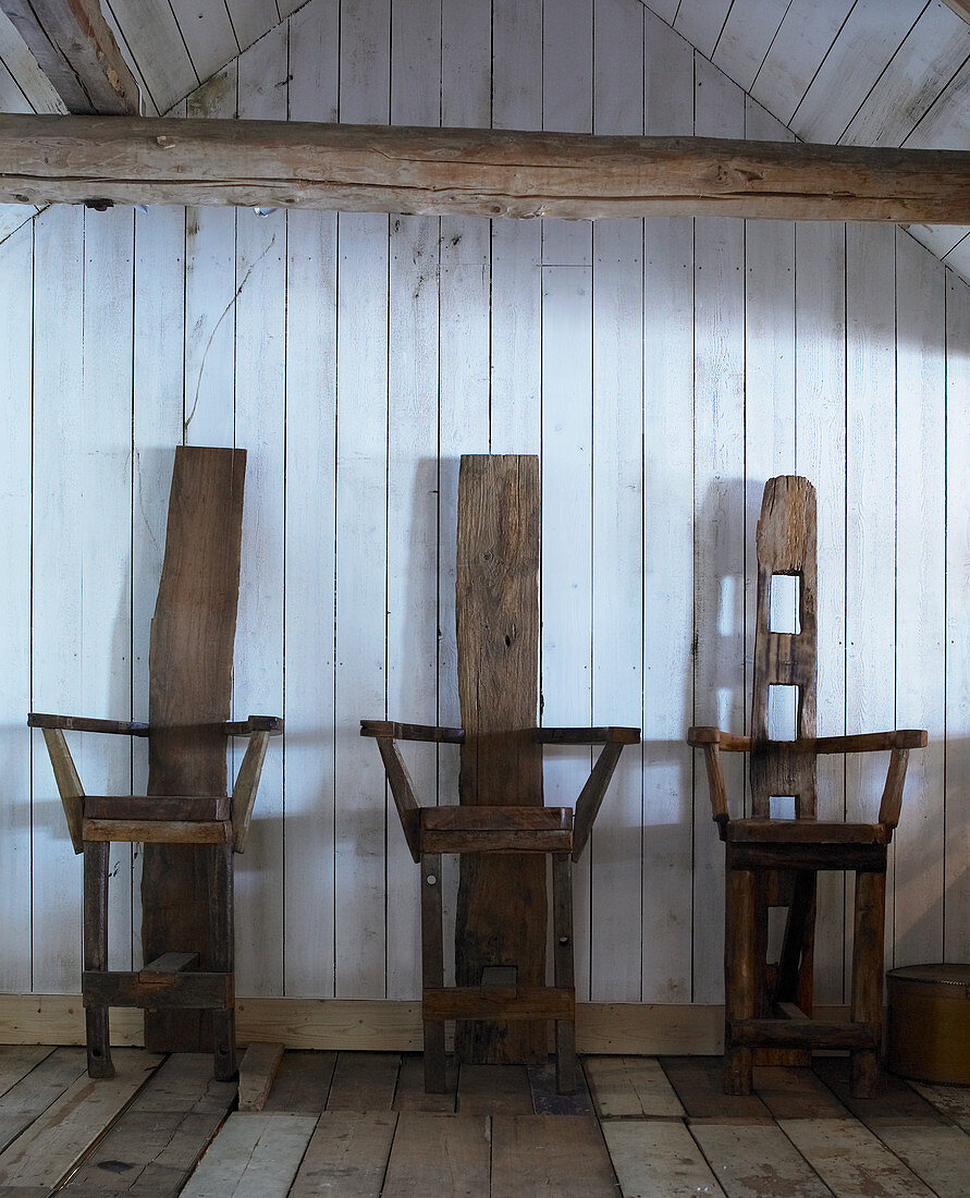 Three chairs made from reclaimed wood against board wall in wooden house