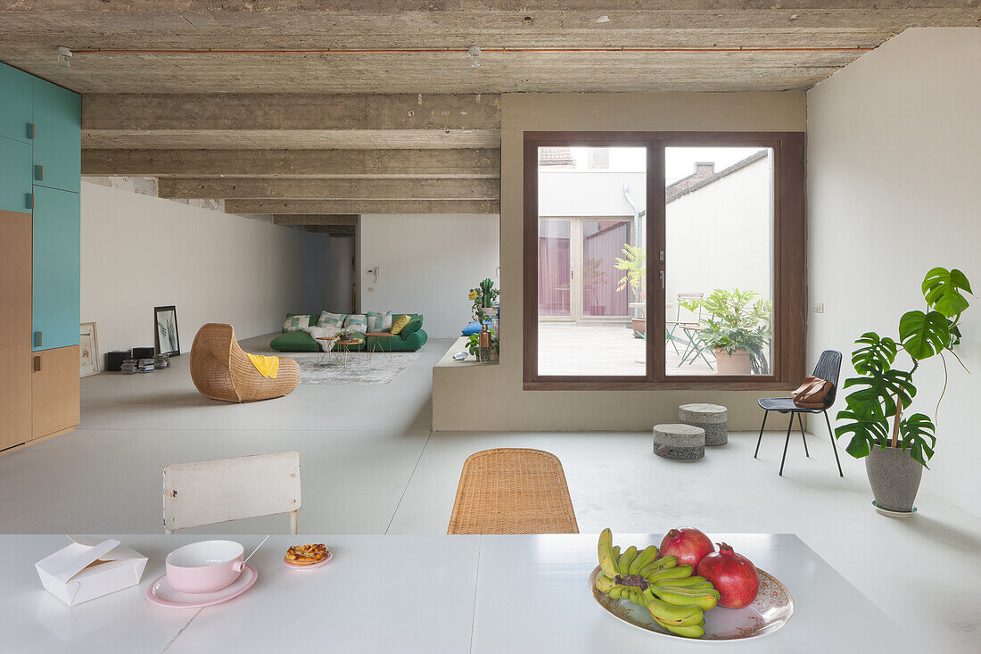 Minimalist, open-plan living room with concrete ceiling and large window overlooking the courtyard