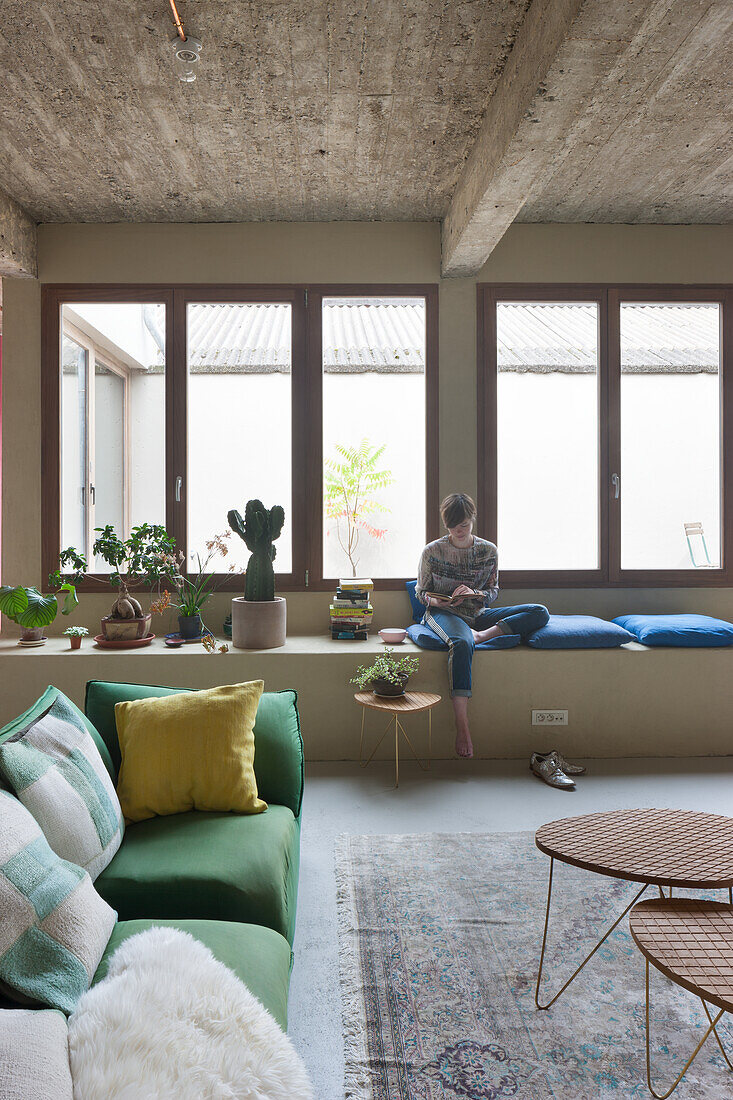 Wohnzimmer mit Betondecke, grünem Sofa und Sitzbereich am Fenster