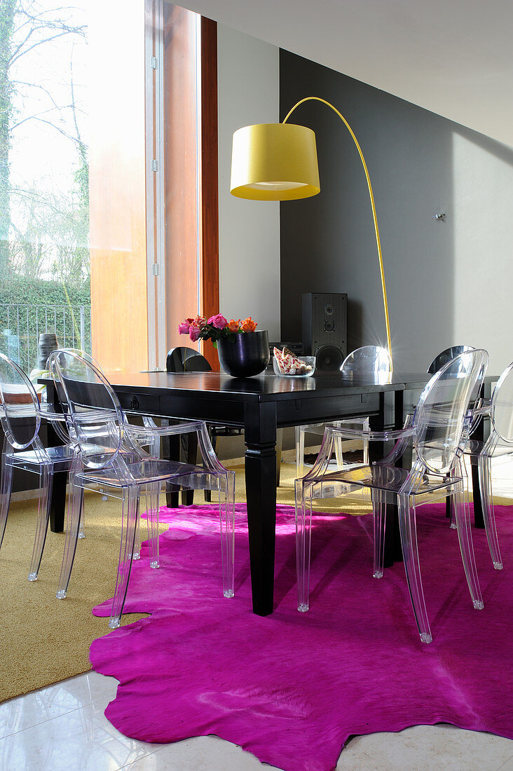 Transparent designer chairs around black table on hot-pink fur rug