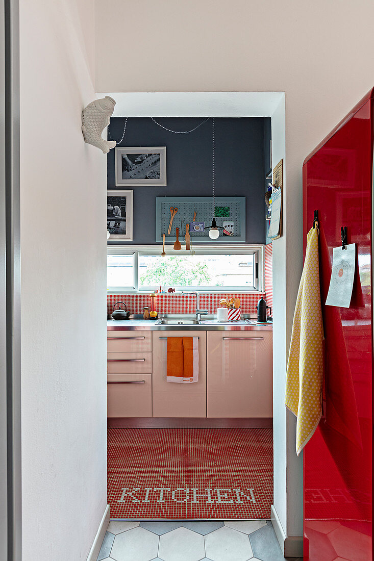 Looking along a red refrigerator into a kitchen with a window strip