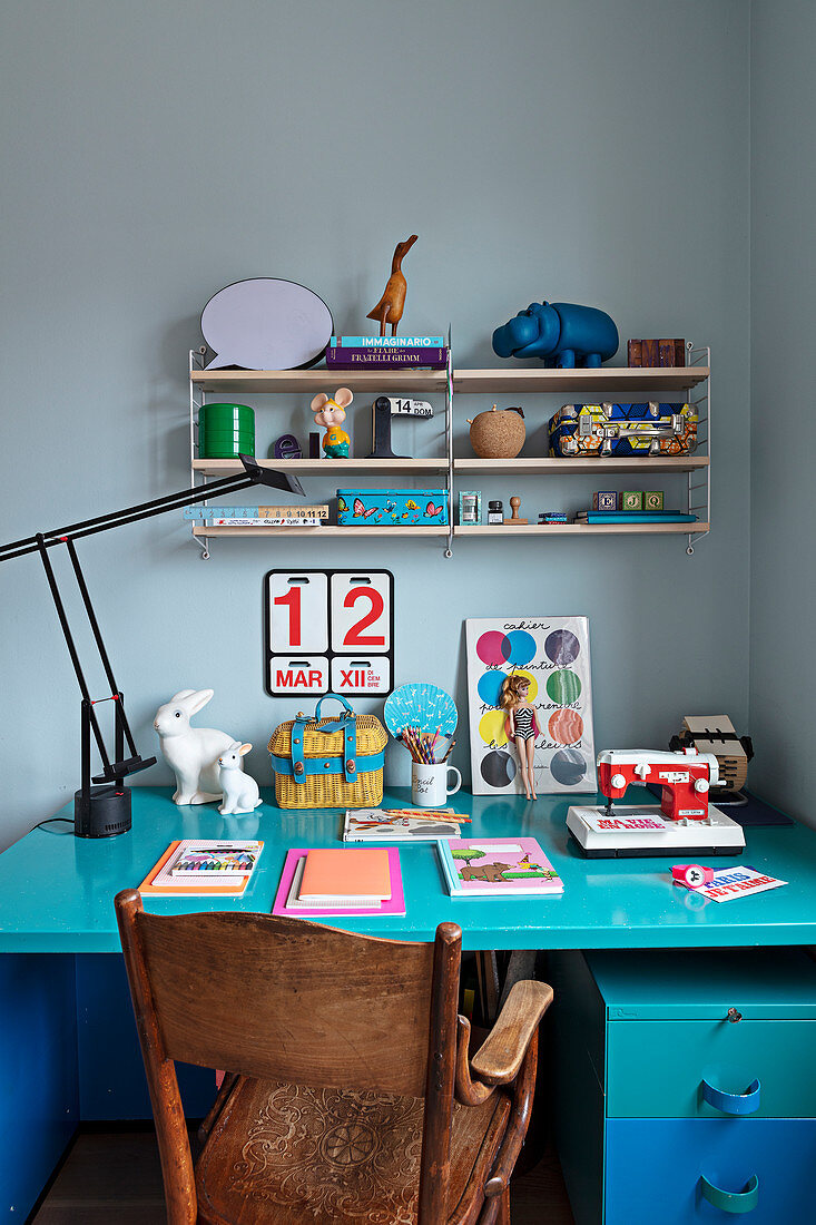 A turquoise-blue desk with a vintage chair and a shelf above it
