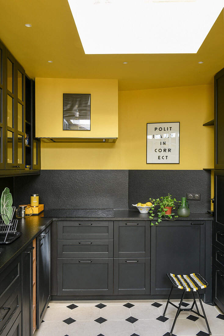 Küche mit schwarzen Möbeln, gelber Wand und Decke und Dachfenster