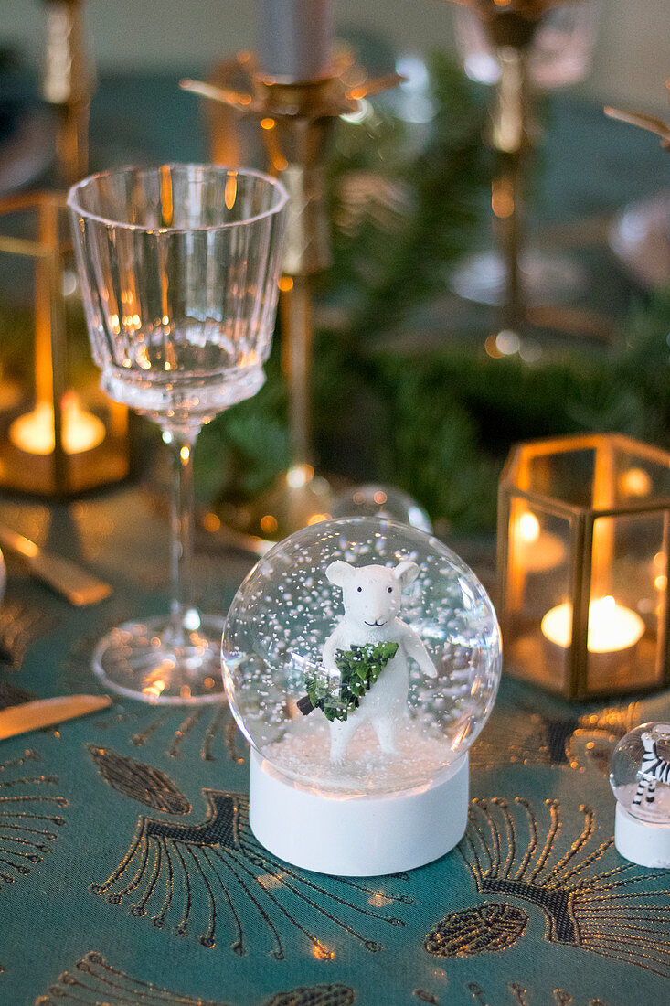 Weiße Maus in einer Schneekugel auf weihnachtlich gedecktem Tisch