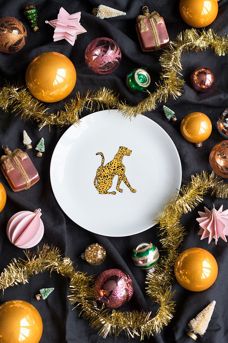 Plate with leopard motif on black fabric surrounded by Christmas-tree baubles