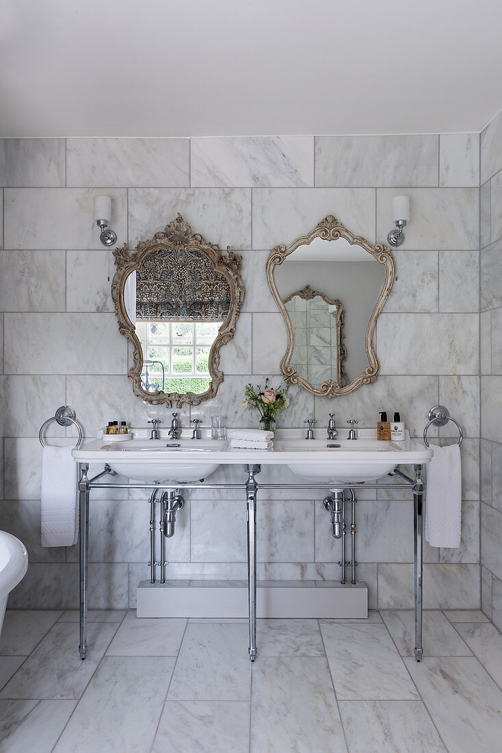 Decorative 1930s Art Deco-style mirrors above double sinks in a marble bathroom