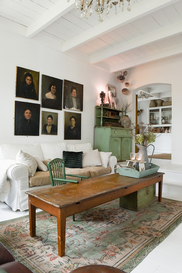 Alter Holztisch, helles Hussensofa und Portraitmalerei im Wohnzimmer